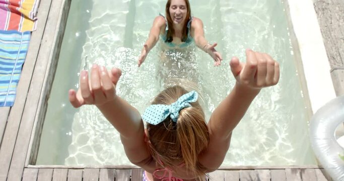 Happy caucasian mother playing with daughter and jumping into swimming pool