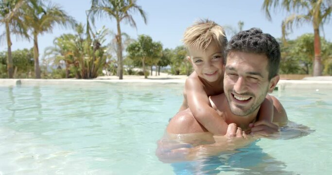 Portrait of happy caucasian father carrying his son in swimming pool