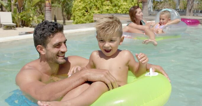 Portrait of happy caucasian family playing with inflatables in swimming pool