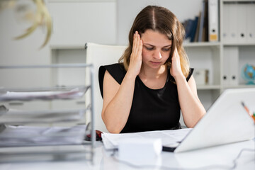 Exhausted female office worker sitting at desk. Tired woman accountant doing her job.