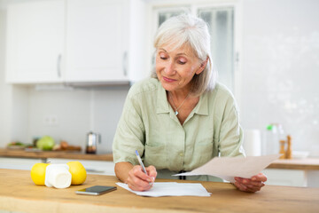 Cheerful old woman writing on paper, calculating bill payment.