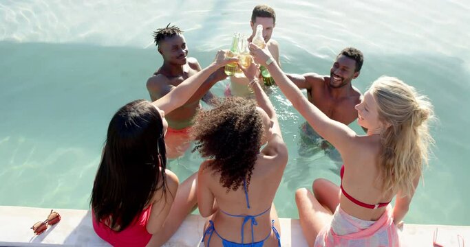 Happy diverse group of friends drinking beer and cheering at pool