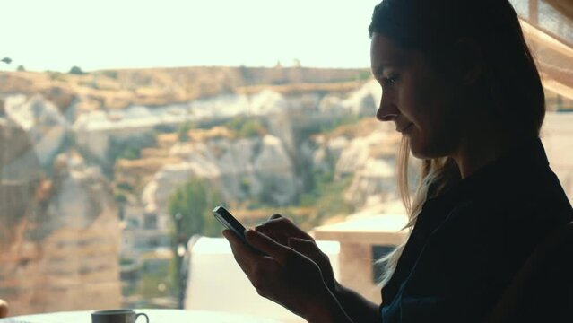 Side-view of beautiful woman texting on smartphone and smiling at the message with beautiful view in background
