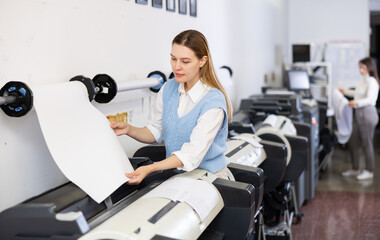 Woman working in publishing facility, loading large format paper in printer.