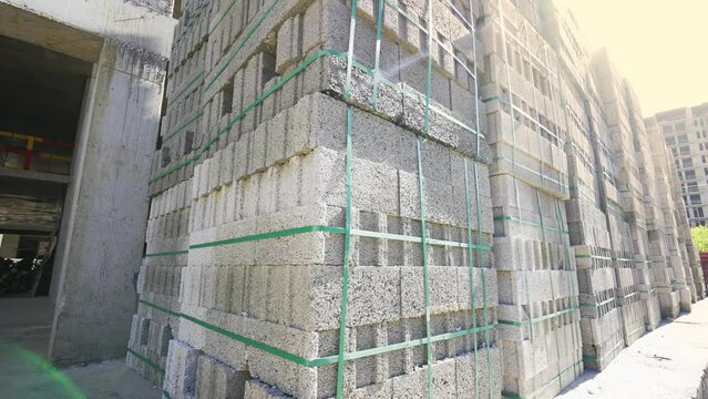 Large stack of pumice blocks and blocks packed on pallets in form of cube. Construction site, camera moving, large number of blocks against background of construction and sunlight.