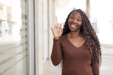afro pretty black woman smiling happily and cheerfully, waving hand, welcoming and greeting you, or saying goodbye