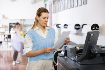 Fototapeta premium Female employee of the printing house adjusts the plotter using a computer