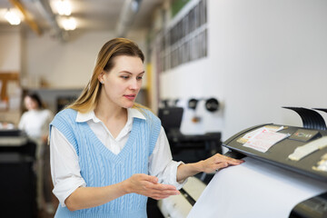 Woman employee of printing house puts a sheet of paper into a plotter