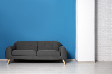 Stylish grey sofa near blue wall in room. Interior design