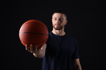 Obraz premium Athletic young man with basketball ball on black background, selective focus