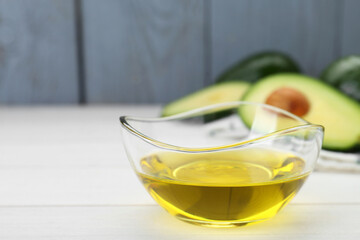 Bowl with avocado oil on white wooden table, closeup. Space for text