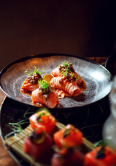 round plate of sushi with rolled salmon and vegetable decoration, with dark background and soft light on the plate