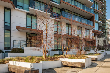 Facade of a modern apartment building. Recreation area with empty wooden benches. Urban modern public city resting area
