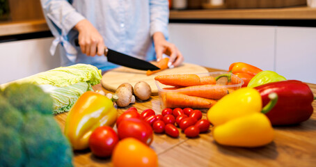 Girl cuts tomatoes for a salad on the board on a wooden table , surrounded by fresh vegetables , zucchini , green beans , cucumbers ,