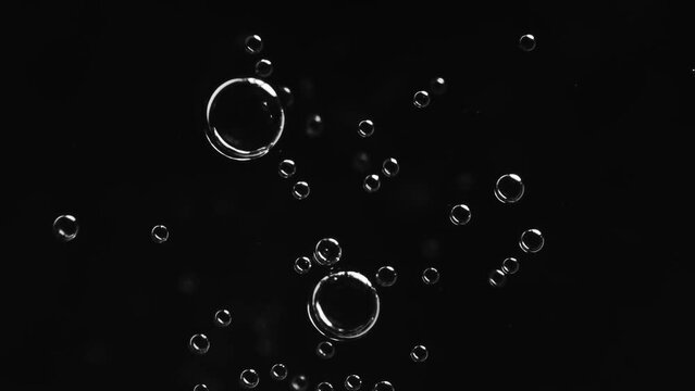 Top view closeup scene on small bright white bubble fuse together to be a bigger and break isolated on black background, fizz texture of soda water when gas release