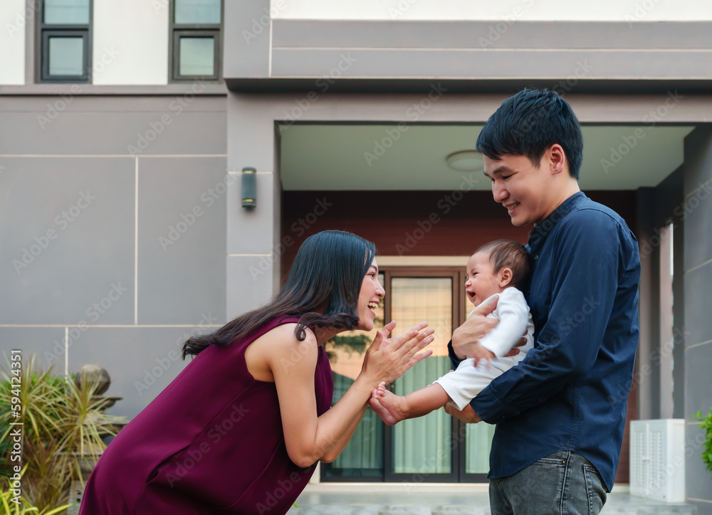 Wall mural happy family, cheerful father and mother holding and playing with newborn baby while standing in fro