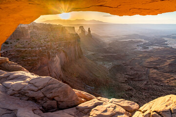 Fototapeta na wymiar A phenomenal landscape scene of a rock opening with view of distance mountains and cliffs back illuminated by the rising sun, Mesa Arch at sunrise, Island In the Sky, Canyonlands, Utah