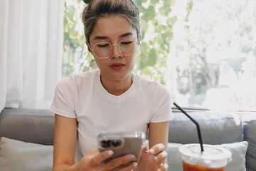 Asian cute girl texting on the phone while having a dessert in the cafe.