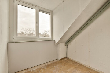 an empty room with wood floors and white walls, looking out to the street from under the stairs on the second floor