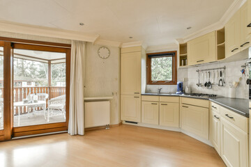 a kitchen with wood flooring and white cupboards, doors open to the outside patio area looking out onto an outdoor deck