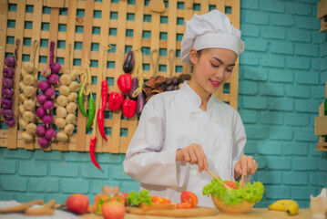 Beautiful asian female professional chef stirring bowl of fresh green vegetables with a spatula in kitchen full of cooking ingredients.