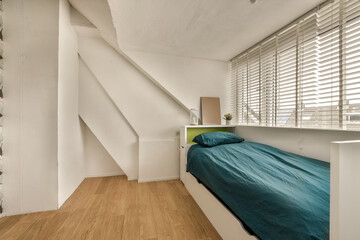 a bed in a room with wooden flooring and white shutters on the wall behind it is a window