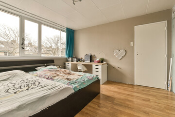 a bedroom with a bed, desk and window overlooking the cityscapearn com logo on the comforter