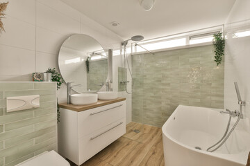 a modern bathroom with wood flooring and green tiles on the walls, along with a freestanding bathtub