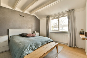 a bedroom with a bed, window and wooden bench in the middle of the room there is a lamp on the wall