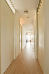 a long hallway with white walls and wood flooring on both sides, leading to an open door that leads to another room