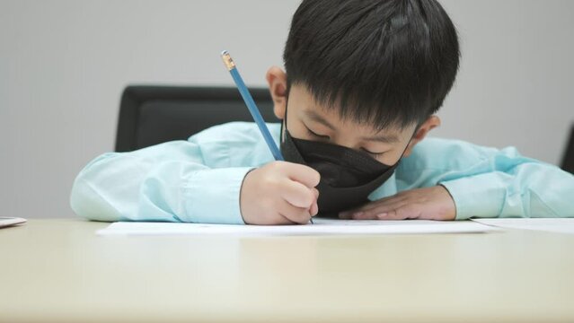 Asian boy wearing formal shirt and chemical face mask writing a test or exam for entering school.
