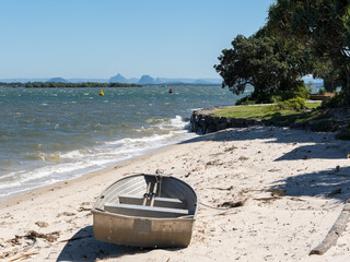 Boat on the sandy beach on Bribie Island with a view across Pumicestone Passage to the glasshouse Mountains on the horizon, Queensland, Australia