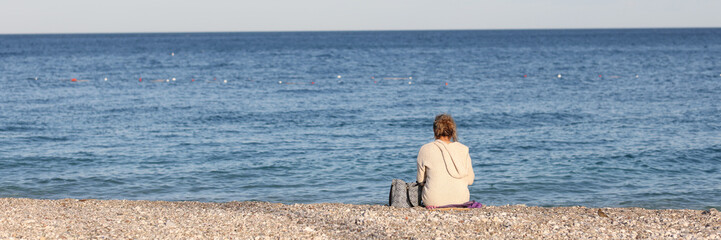 Fototapeta premium Woman sitting on pebbles beach near sea