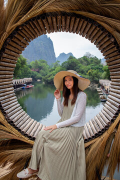Asian women wearing fashionable wicker hats sit on circular bamboo seats against the backdrop of majestic mountains and swamps at Tha Farang, Thakhek, Khammouane Province, Laos.