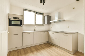 a kitchen with white cabinets and light wood flooring in the middle of the room, there is an oven on the wall
