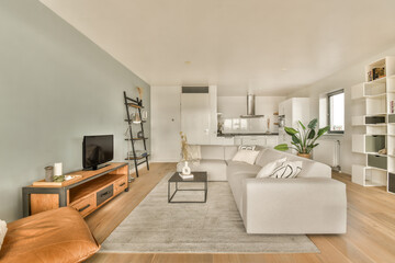 a living room with wood flooring and white couches in the center of the room is an open kitchen