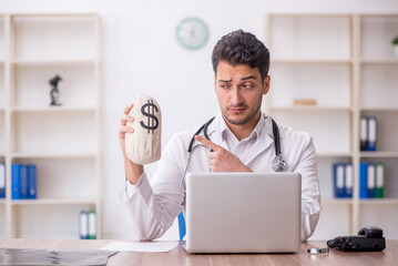 Young male doctor holding moneybag in the clinic