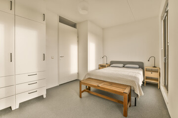 a bedroom with a bed, dressers and cupboards in the corner to the right is an open door