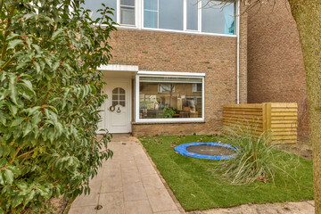 a house with a tree in the yard and some plants growing on the lawn, next to it is a small pool