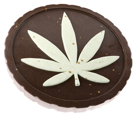 A flat round chocolate brownie with a cannabis leaf shape made of white chocolate