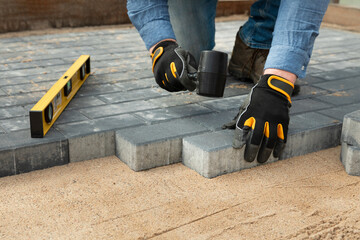 Construction worker laying cement pavement on a walkway with gloves and rubber hammer. House...
