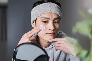 鏡を見ながらニキビの治療やニキビ跡のケアをしているクリームを頬に塗る若い男性