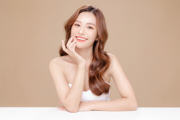Young Asian beauty woman curly long hair with korean makeup style touch her face and perfect skin on isolated beige background. Facial treatment, Cosmetology, plastic surgery. - obrazy, fototapety, plakaty