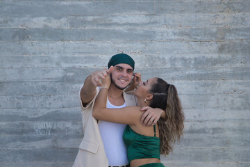 Latin and Hispanic boy and girl couple, young and nonconformist, embracing, while he makes a gun...