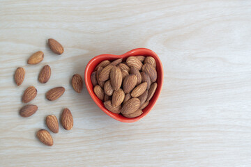 Almonds and Nutcracker, almond nut organic healthy snack vegan vegetarian food. Tasty organic almond nuts snack fruit peeled roasted in heart ceramic bowl on wooden table, top view, copy space.