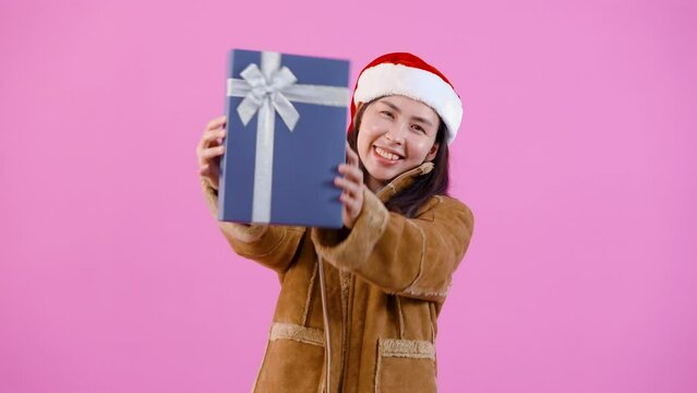 4K woman wearing puffy long sleeve shirt On a cold Christmas night Holding a big blue gift box. hand over the box to the front with a happy smiling face Indoor studio isolated on pink background