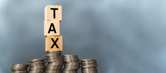 Tax concept with wooden blocks on stacked coins. Word TAX written on wooden cubes on stacked coins on dark background. Panoramic images have free space.