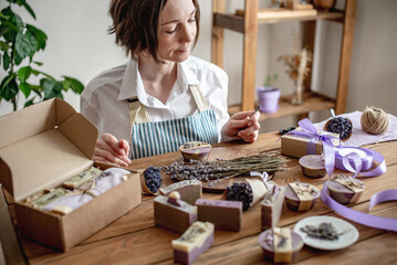 Woman in an apron is packing natural lavender soap and decorating it with lavender flowers. Concept of natural soap and handmade gifts