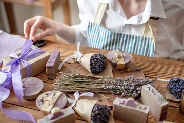 Woman in an apron is packing natural lavender soap and decorating it with lavender flowers. Concept of natural soap and handmade gifts