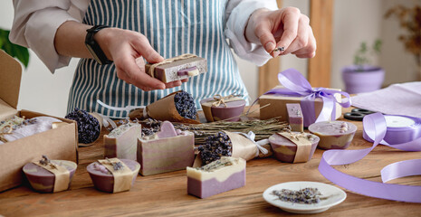 Woman in an apron is packing lavender natural soap and bouquets of lavender flowers. Concept of...